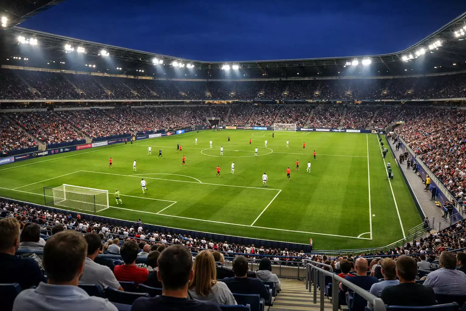 Stade de football vu depuis les tribunes avec un match en cours sous un éclairage puissant